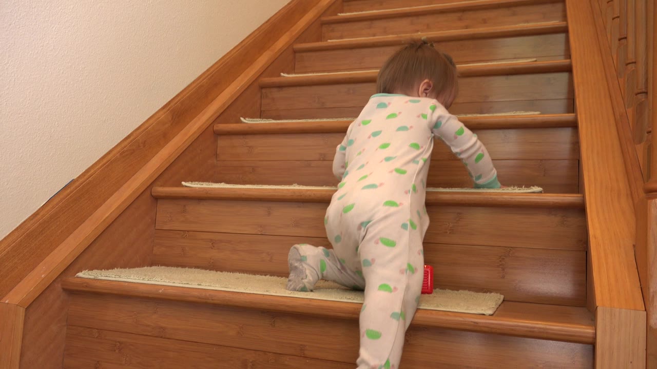 Infant girl climbing onto the next wooden stair.