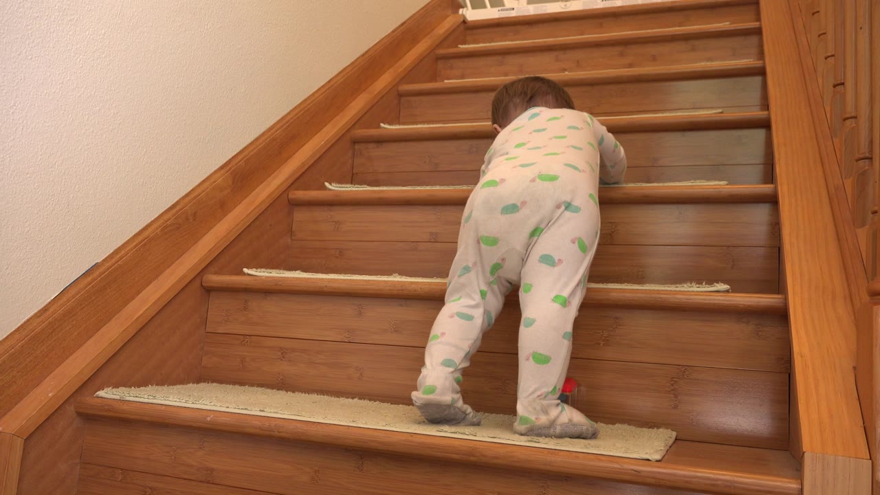 Baby continues crawling up wooden stairs.