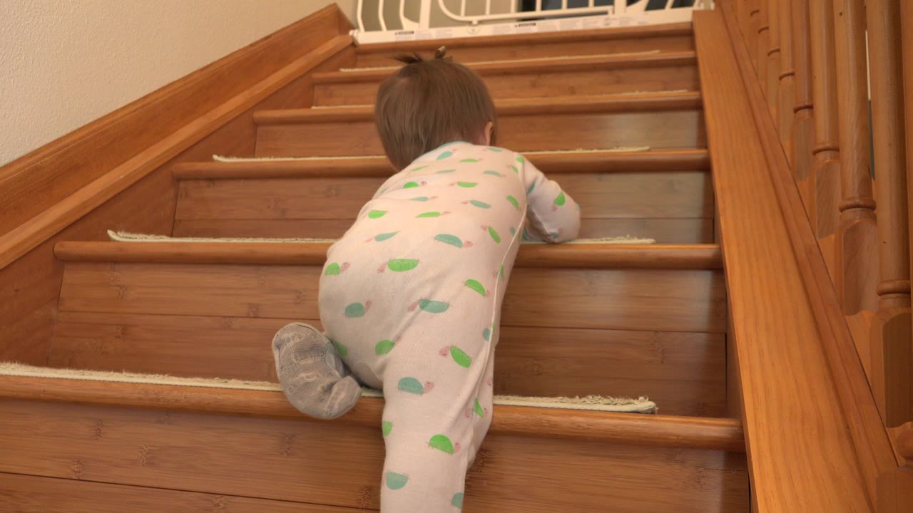 Toddler in footed pajamas crawling up wooden stairs.