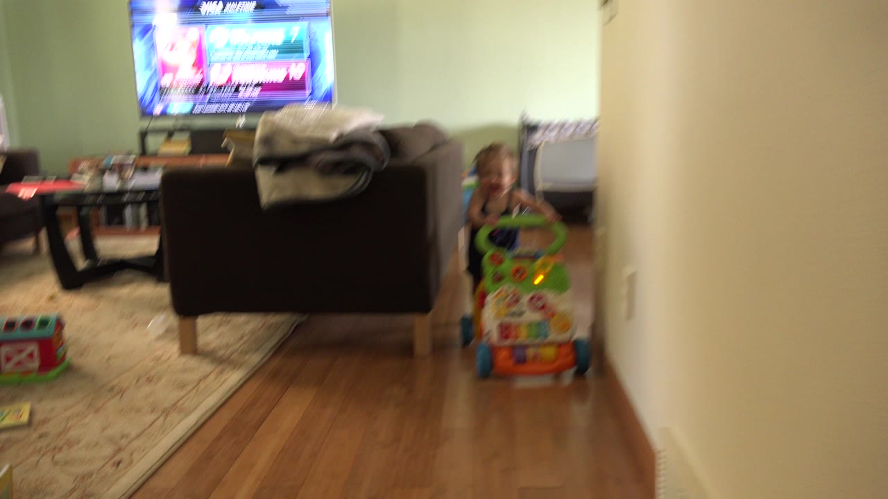 Young child behind a colorful push toy in a living room hallway view.