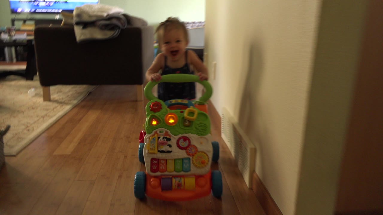 Baby behind a colorful toy walker in a hallway