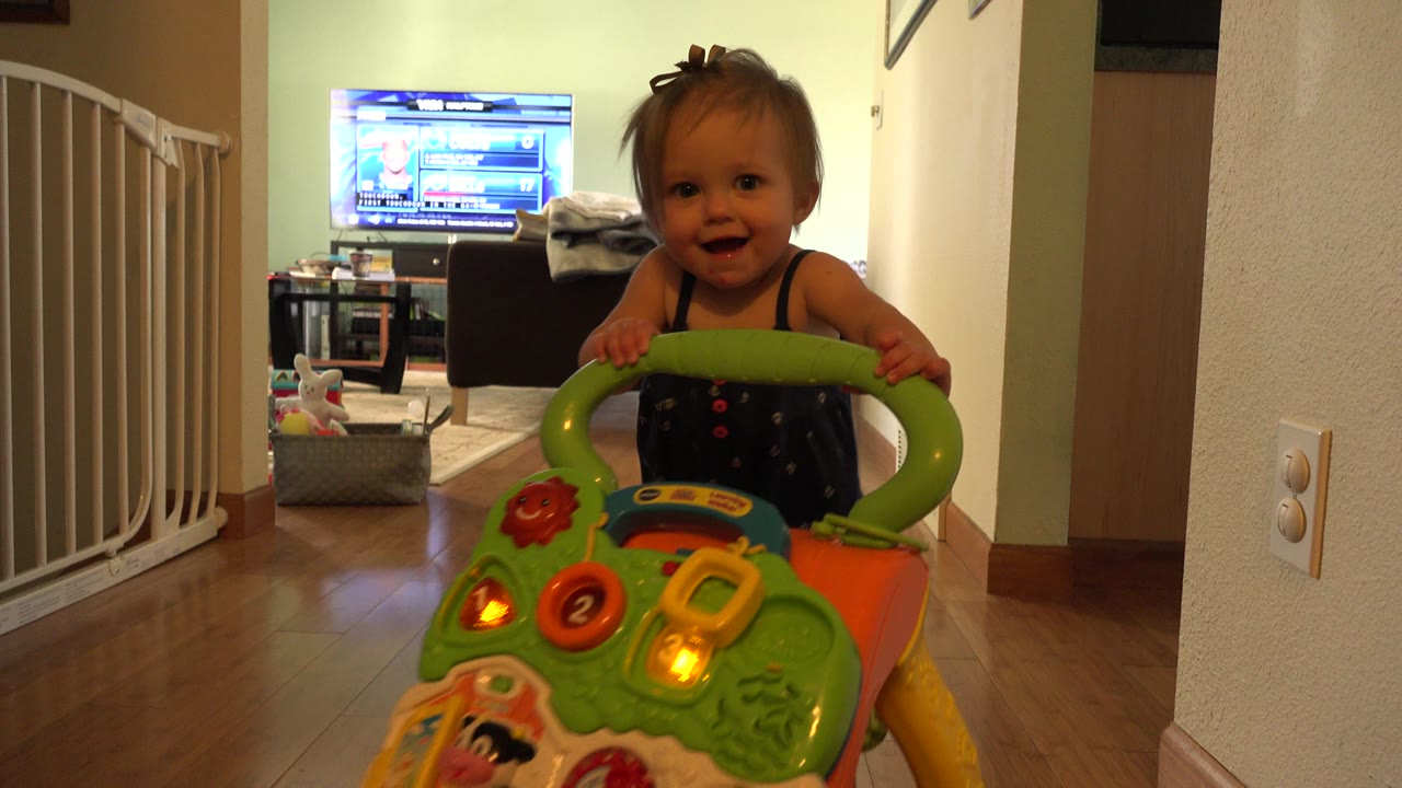 Toddler behind a bright push toy in a hallway.