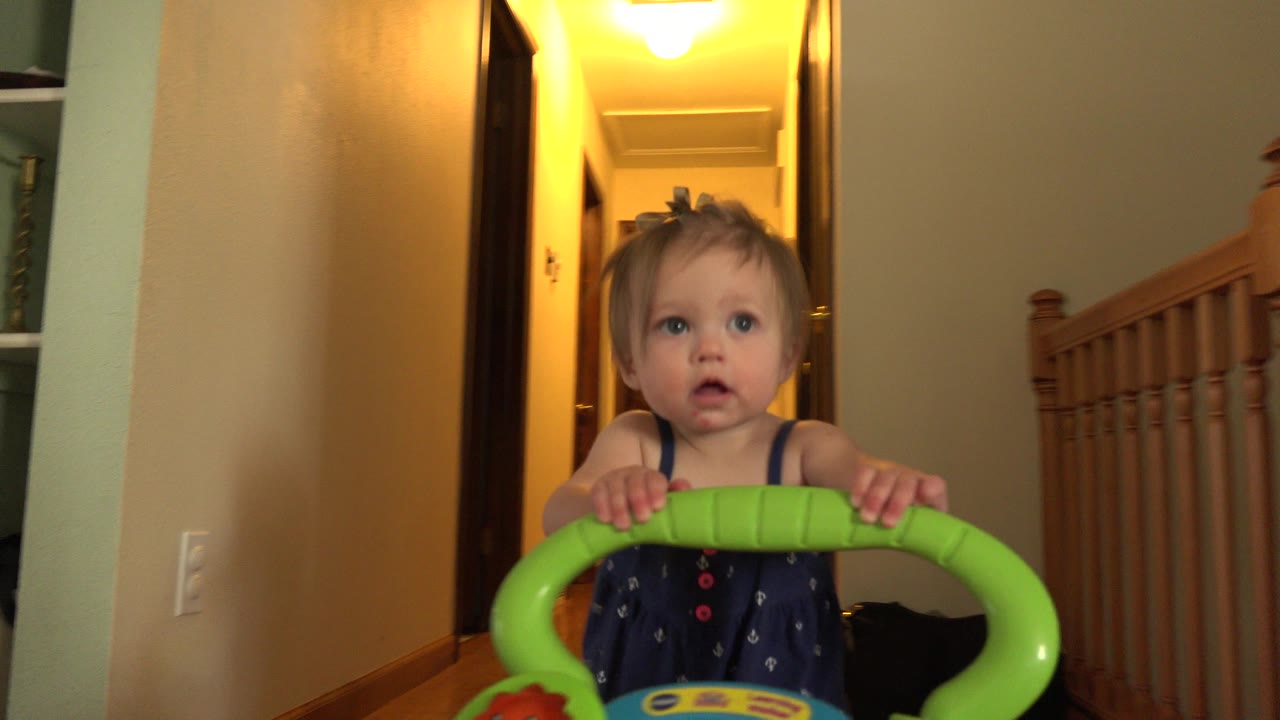 Toddler holding a green walker in a warm hallway.