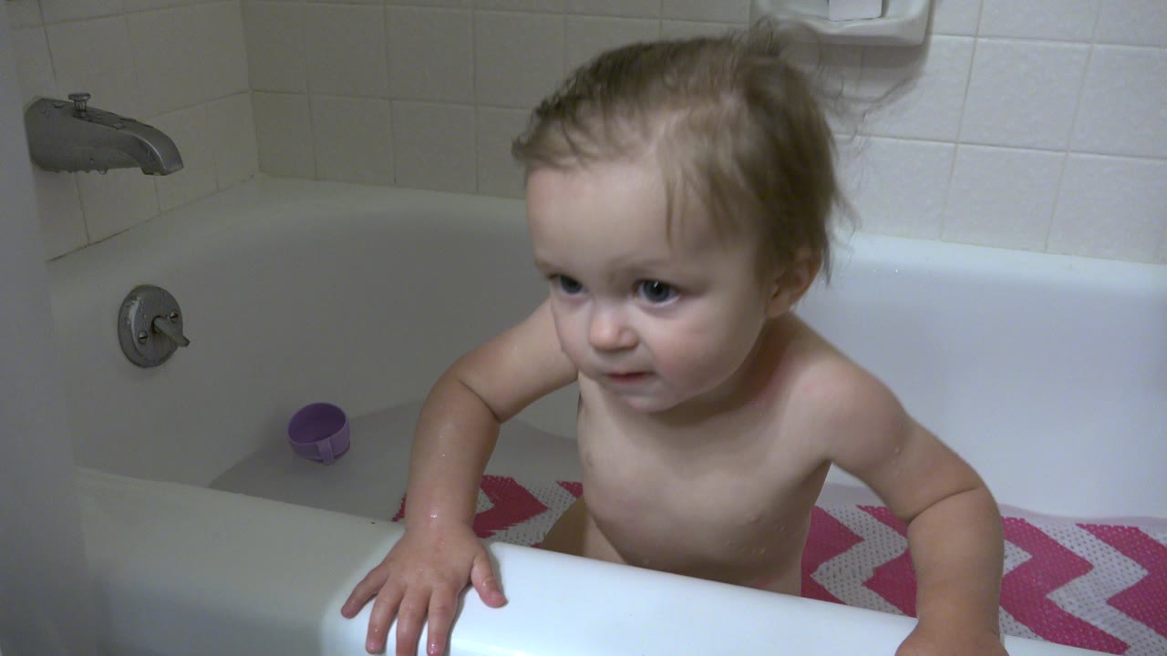 Young child standing in a bathtub and looking left.