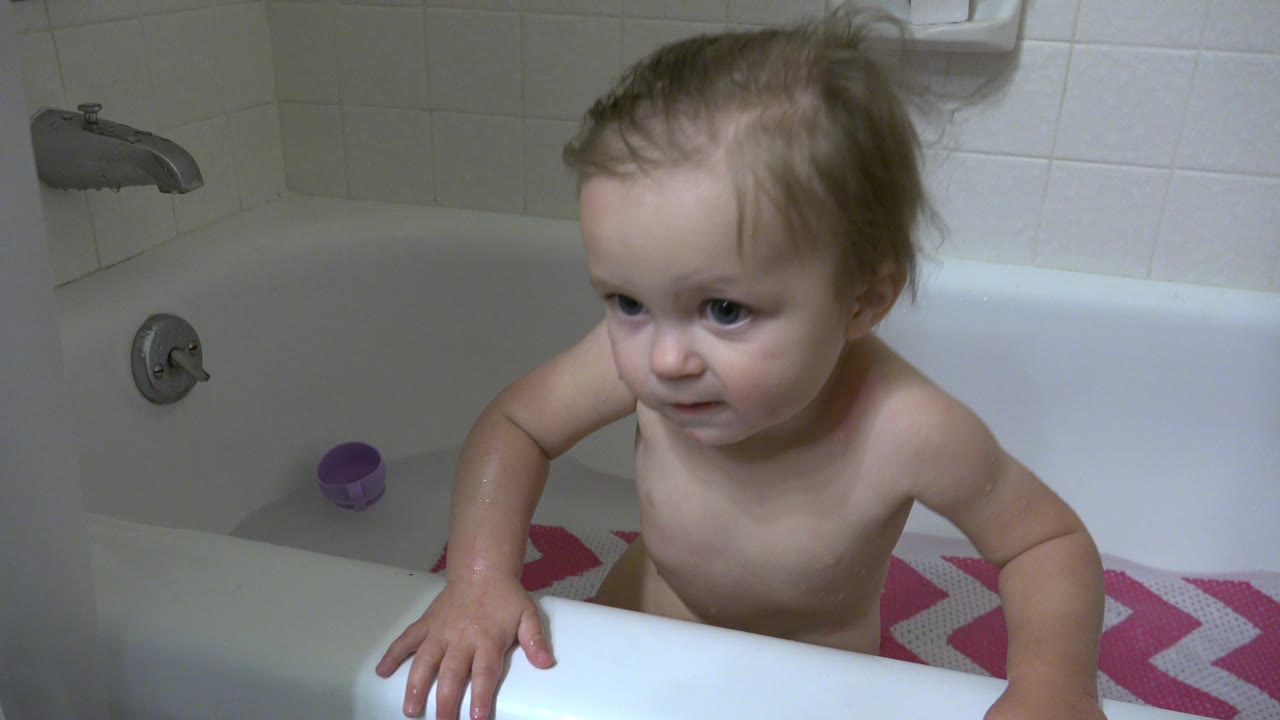 A wet young child in a Westminster, Colorado bathtub holds the tub edge with one hand while looking off to the side, with bathroom tile and fixtures in view.