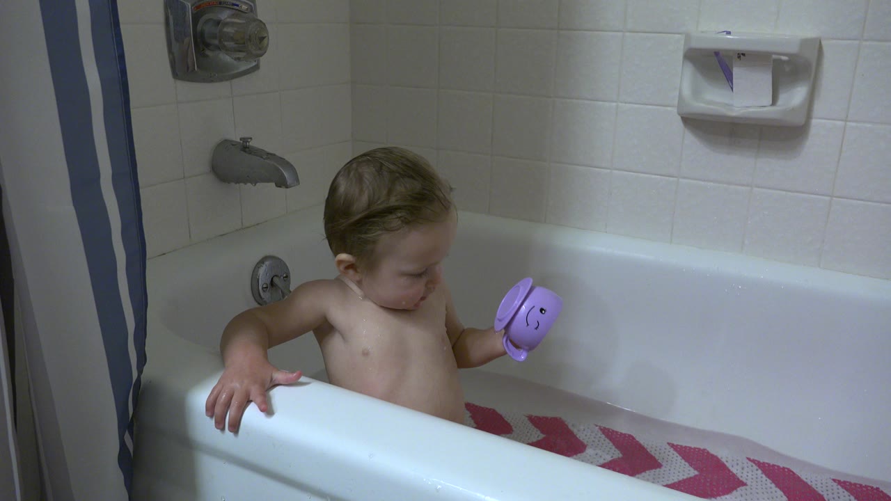 Small child in a bathtub holding a purple bath toy.