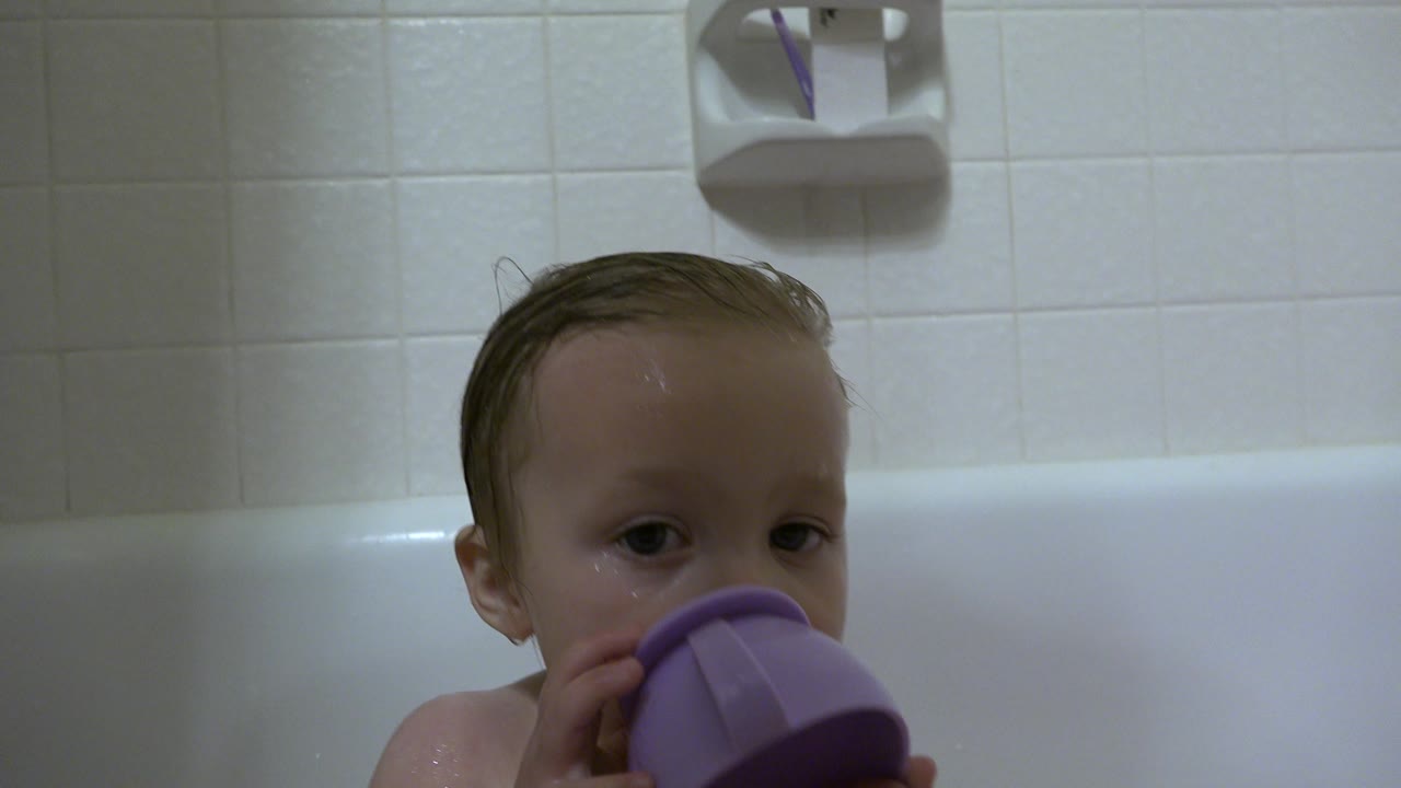 Baby boy in a bathtub partly hidden behind a purple cup.