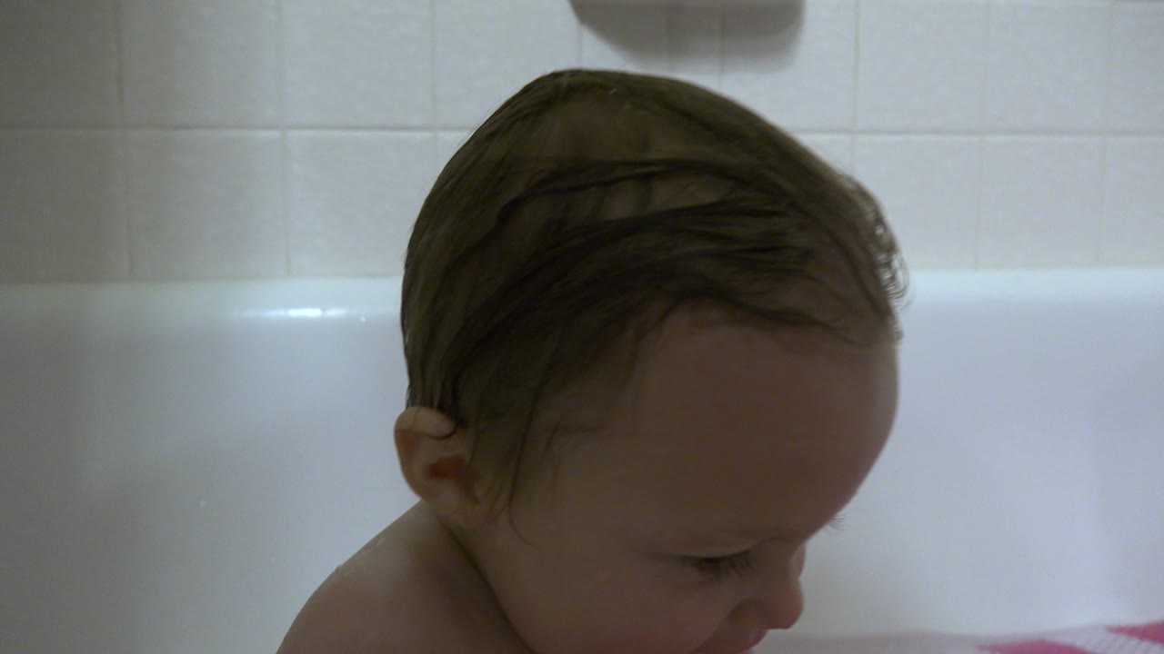 Toddler with wet hair seated in a white bathtub.
