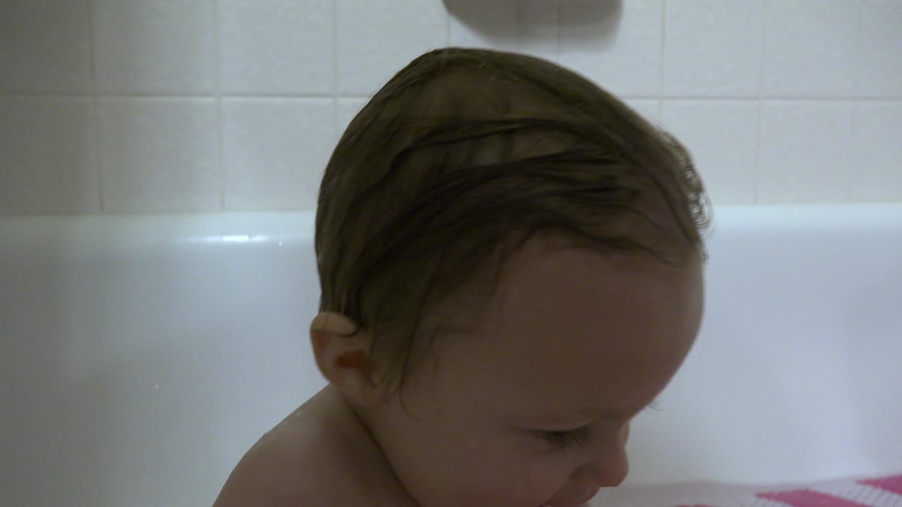 The child remains seated in the bathtub in Westminster, Colorado, head bowed slightly, with wet hair against the light tile background.