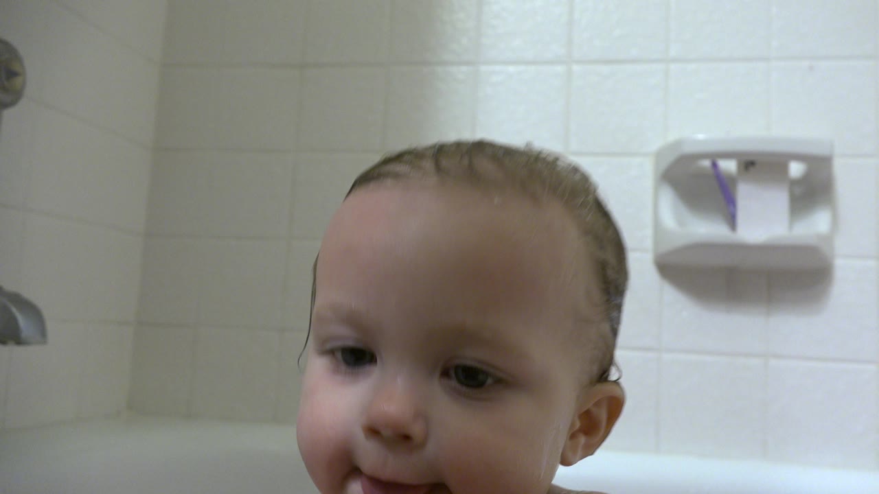 Baby's head above a white bathtub rim in a tiled bathroom.