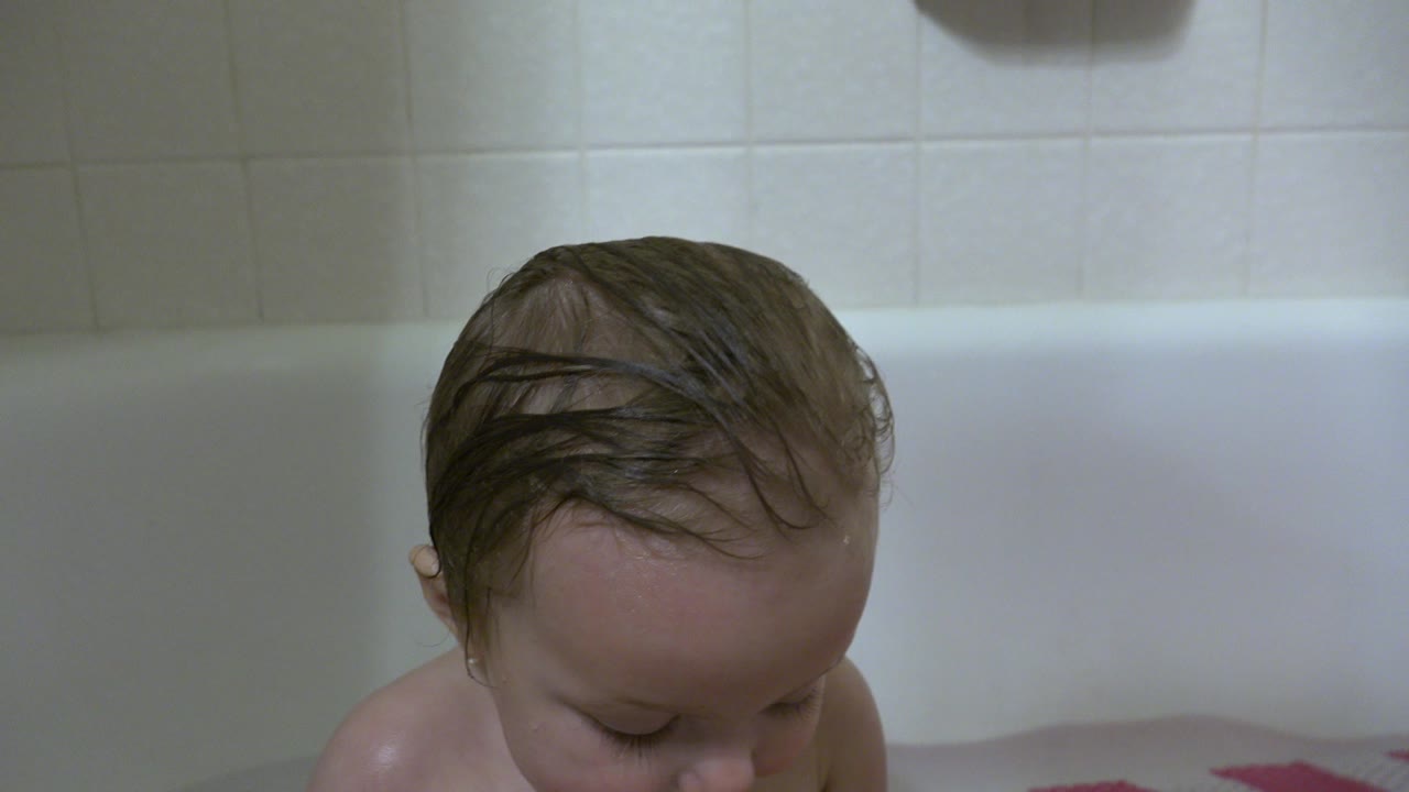 At 0:00, a wet-haired baby looks down inside a white bathtub in Westminster, Colorado, with pale tile and soft bathroom light behind the child.