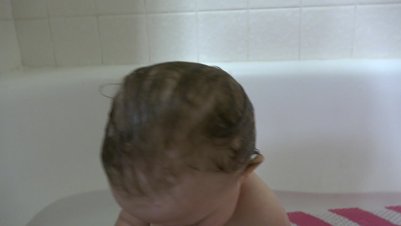Top of a baby's wet head near the side of a bathtub.