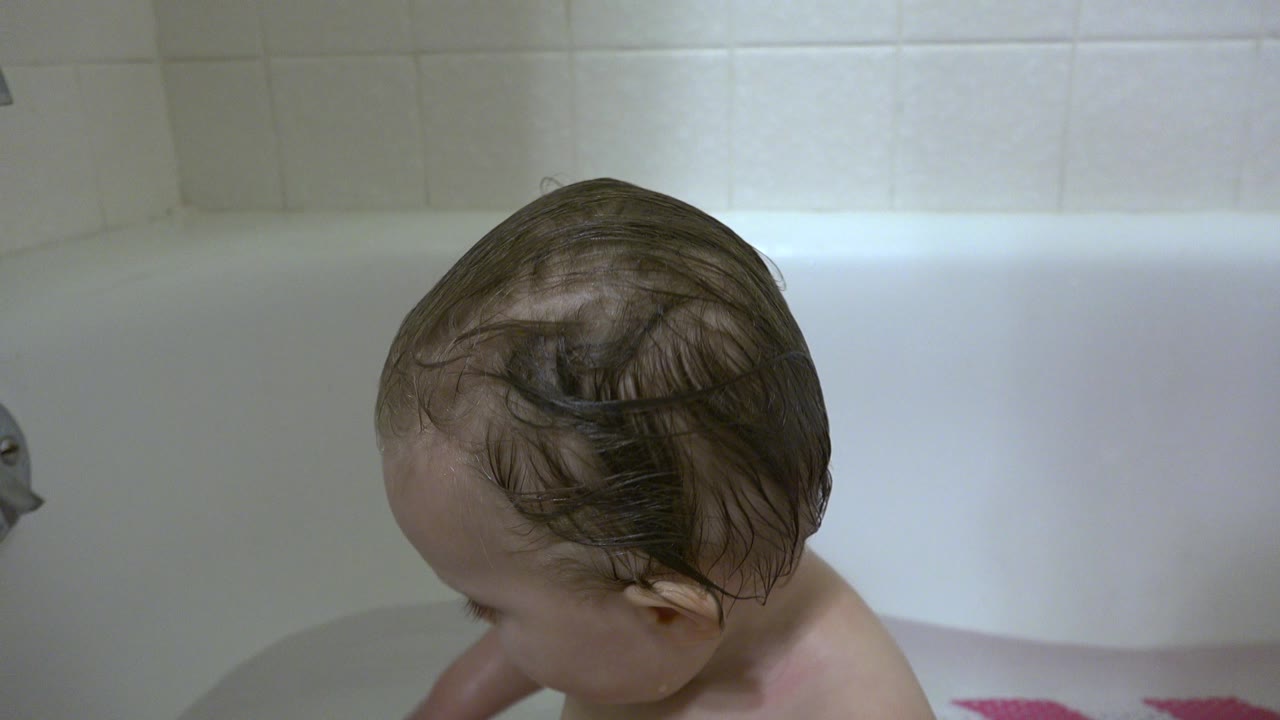 Baby with wet hair sitting in a white bathtub.