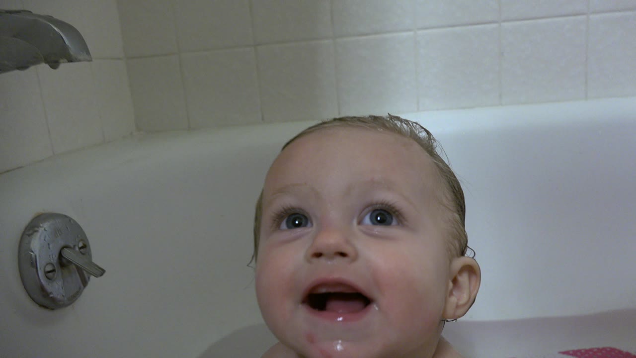 The baby remains low in the bathtub, looking upward as the tub handle and white tiled wall sit in the background of the Westminster, Colorado home interior.