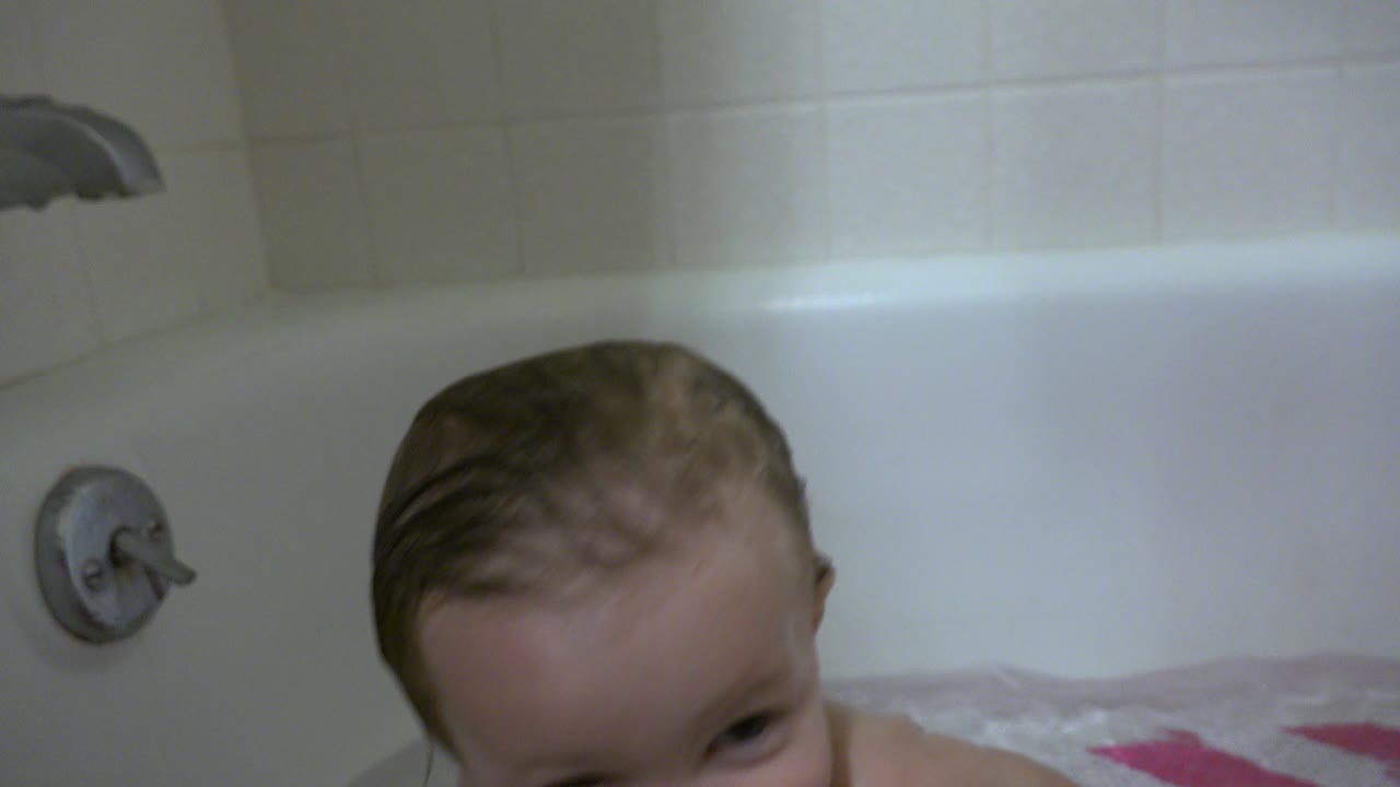 At 0:01 in Westminster, Colorado, the infant's wet head rises near the tub rim, with the white tub wall, tile, faucet, and round control in view.
