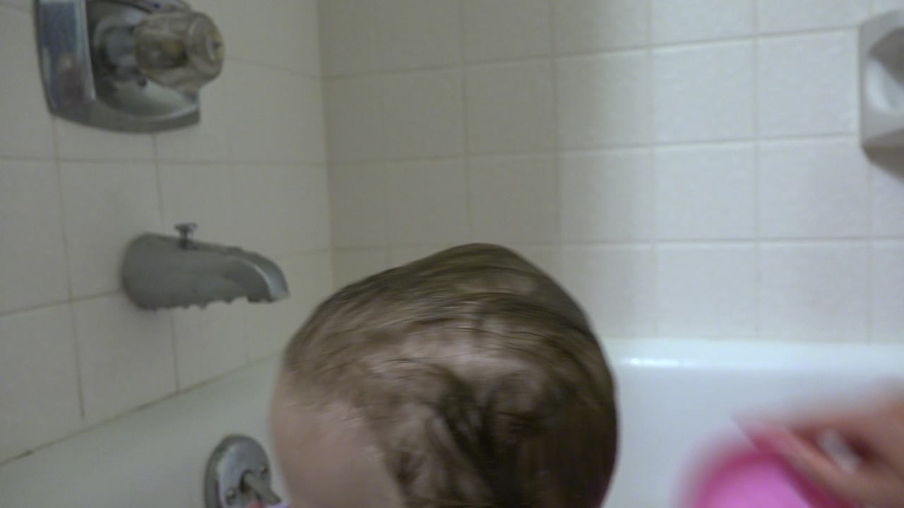 Wet-haired baby partly visible in a bathtub near tile and faucet fixtures.