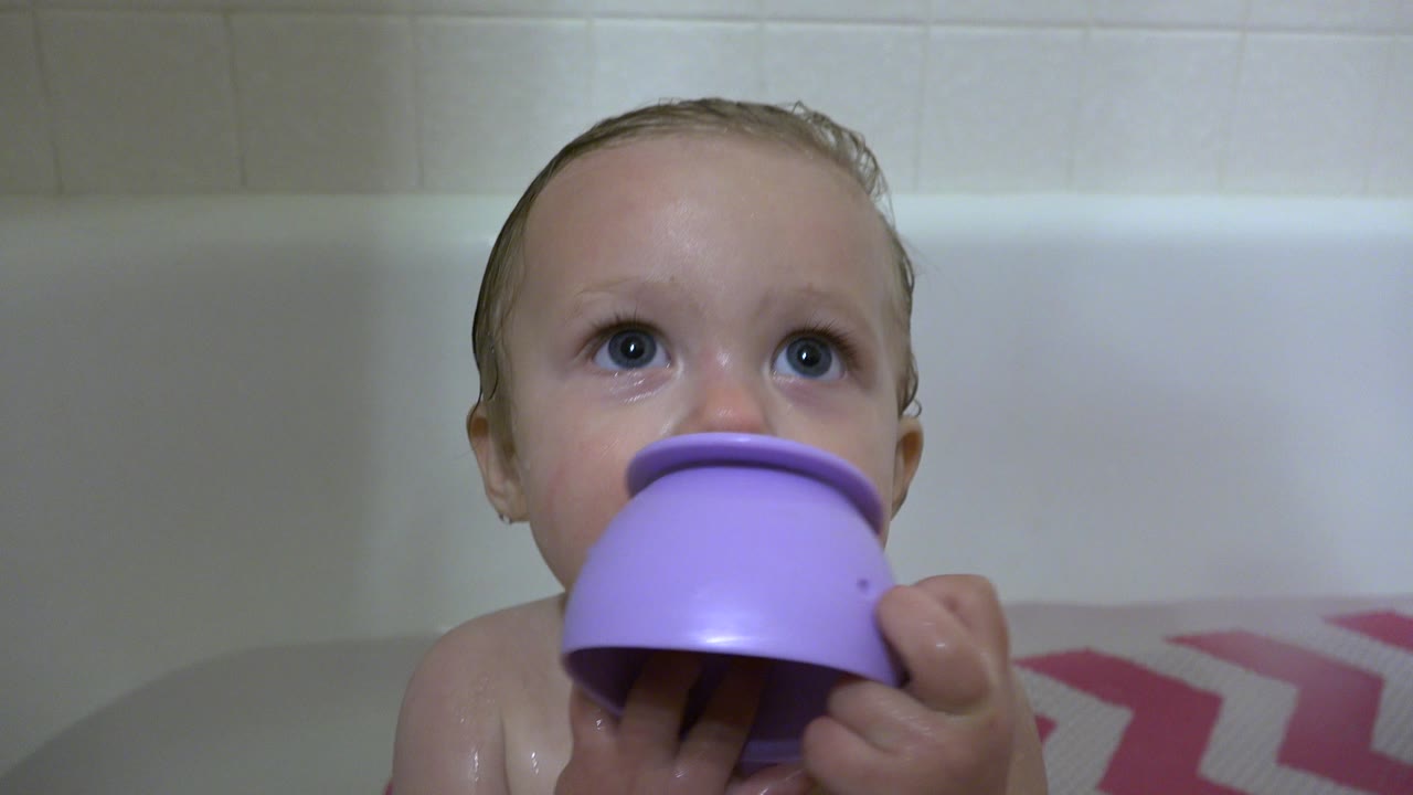 Baby in a bathtub holding a purple toy near their mouth.