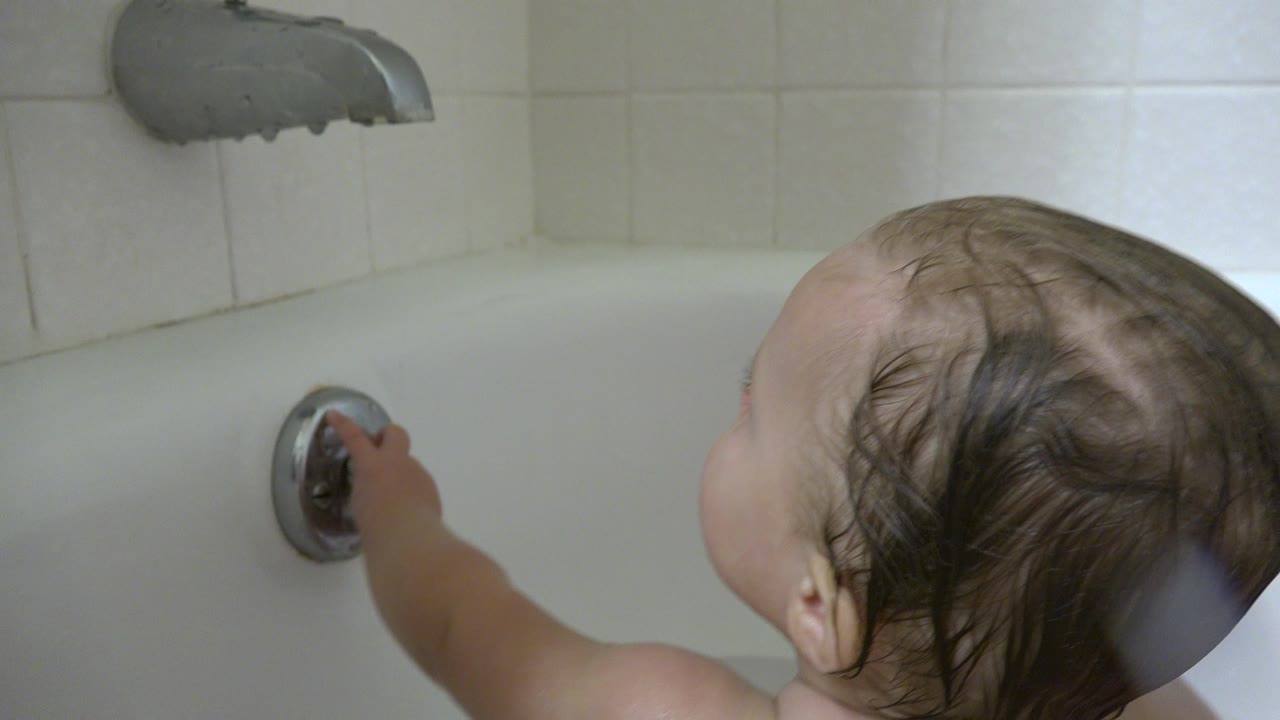 The baby remains turned away in the Westminster bathroom, arm extended toward the chrome handle on the white tub wall.