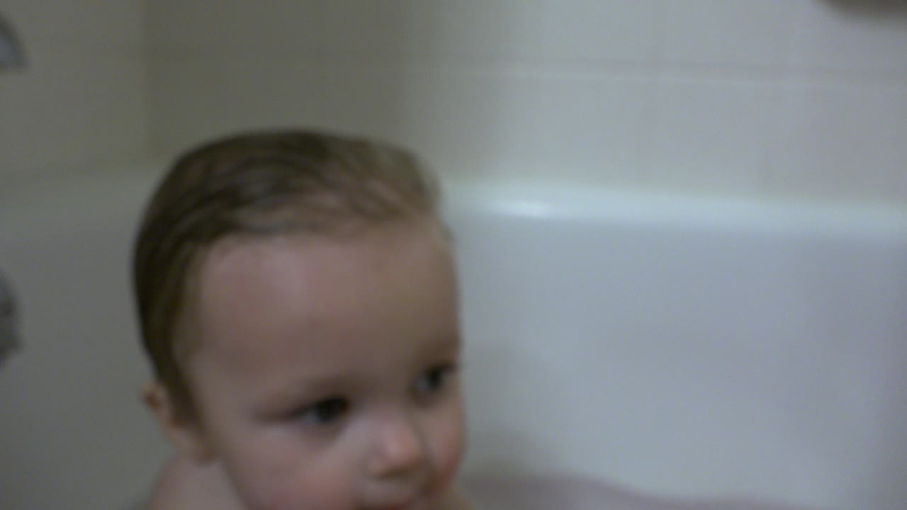 Wet-haired toddler partly visible in a white bathtub.