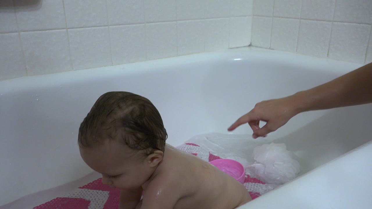 Baby sitting near bubbles and a pink bath cup.