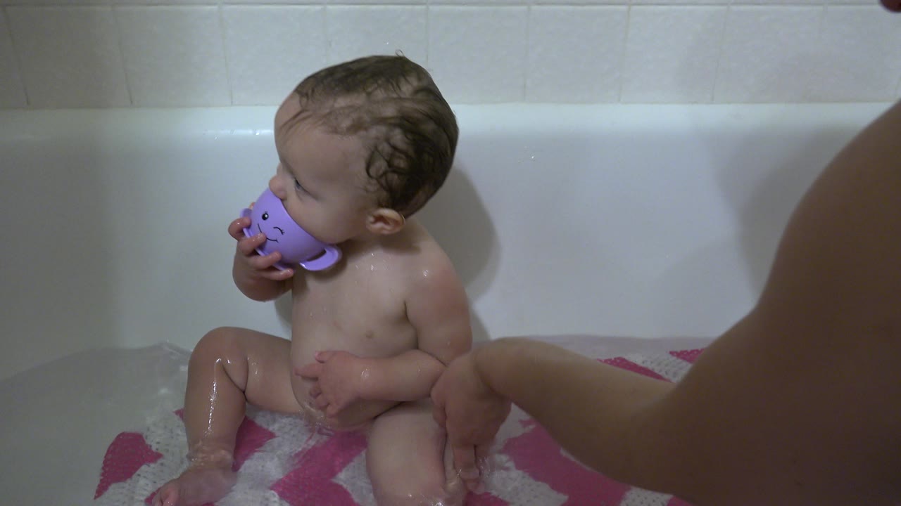 Toddler in a bubble bath holds a purple cup near the face.