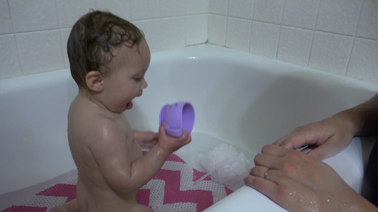 Baby in bathtub holding a purple cup