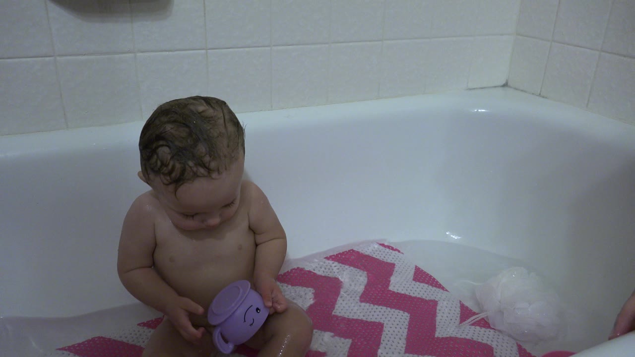 Young child sitting in a bathtub holding a purple toy.