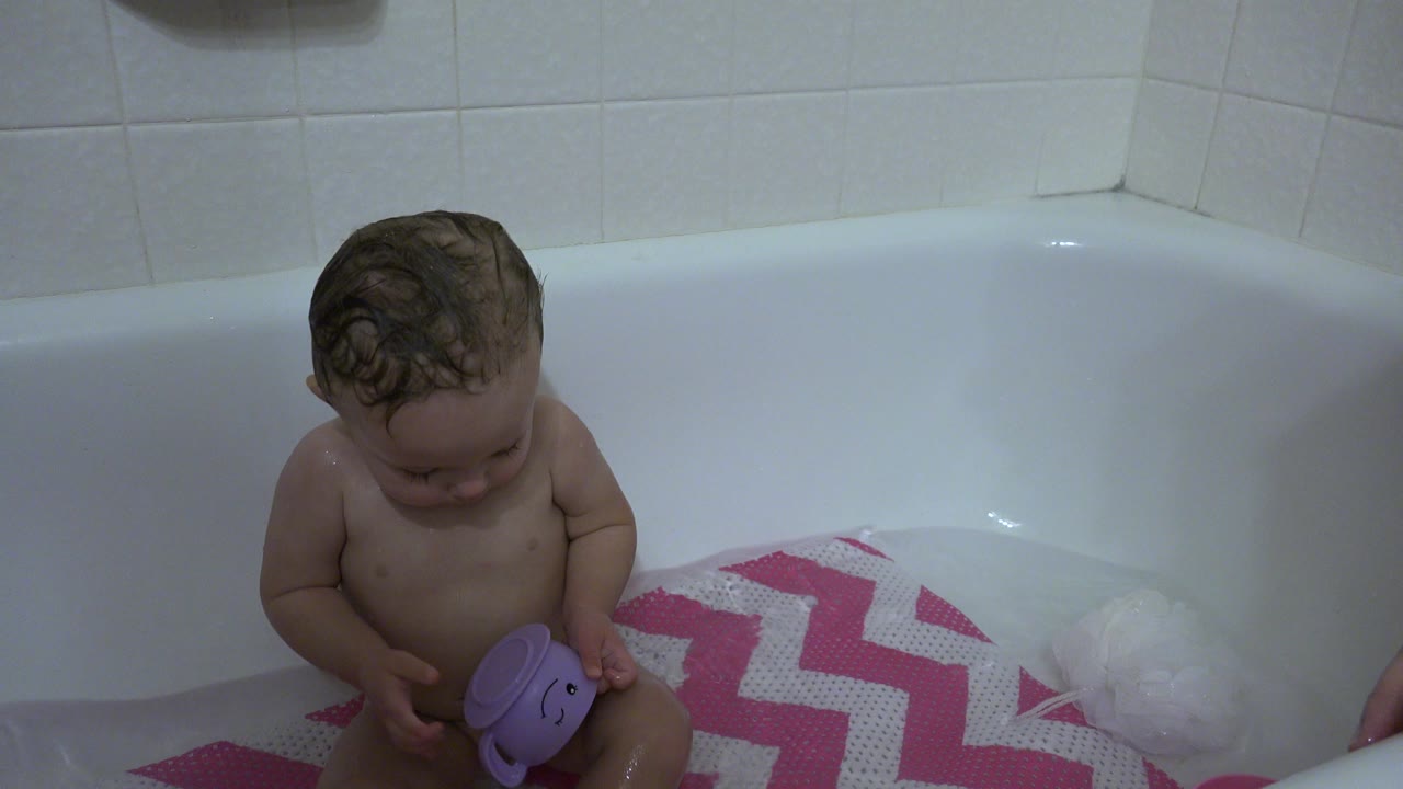 The Westminster, Colorado bathroom scene continues with the child looking down at the purple toy while seated against the white tub and tiled wall.