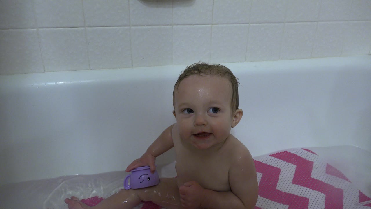 Baby smiling in bathtub beside a purple bath toy.
