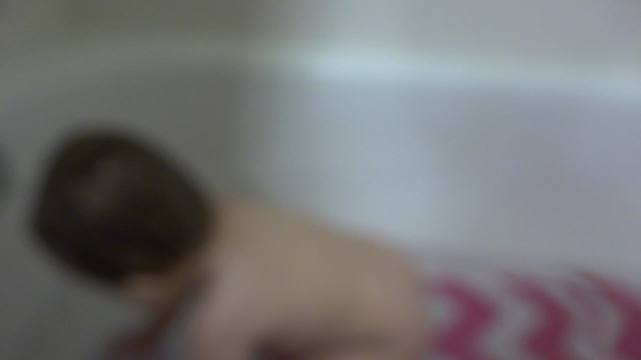 Blurred infant leaning in a white bathtub.