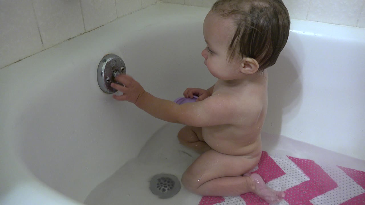 Young child sitting in a bathtub and touching the metal handle.