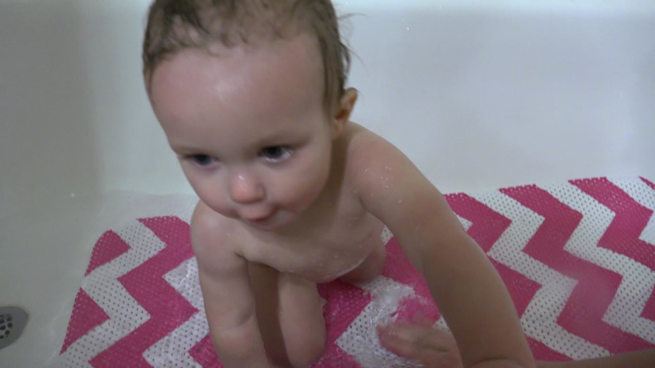 Wet baby sitting in a bathtub on a pink chevron mat.