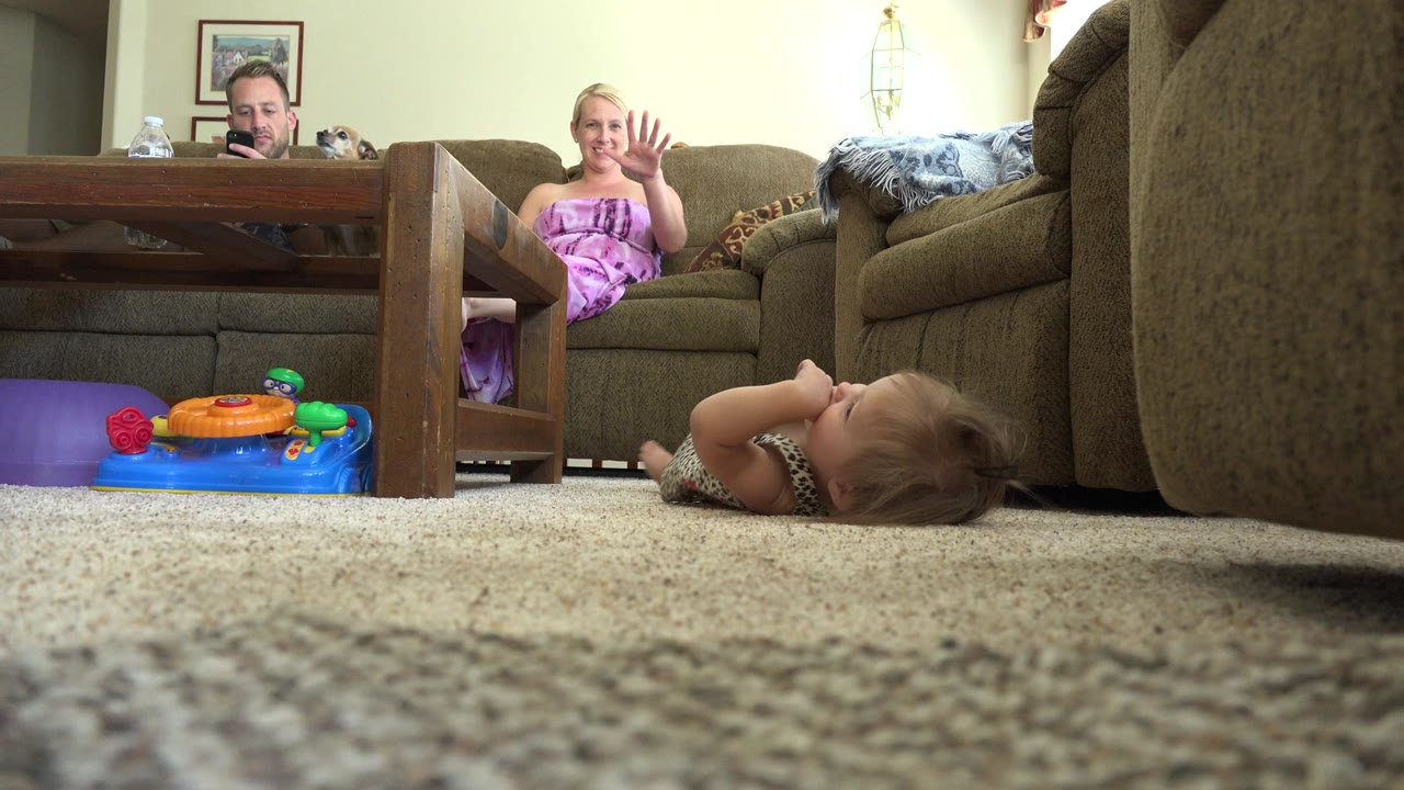Child lying on carpet while adults sit on a couch behind a coffee table.