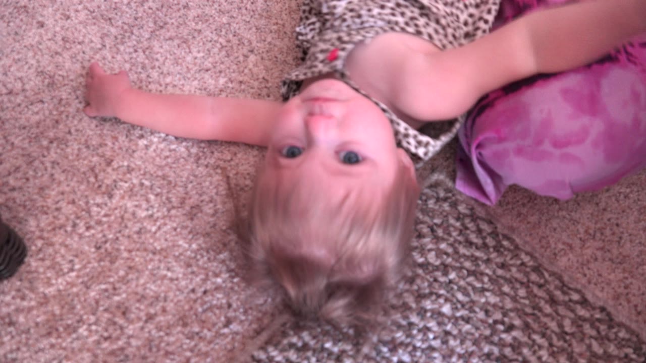 The child remains on the carpet in Westminster, Colorado, with one arm stretched outward and the pink cushion close to her shoulder.
