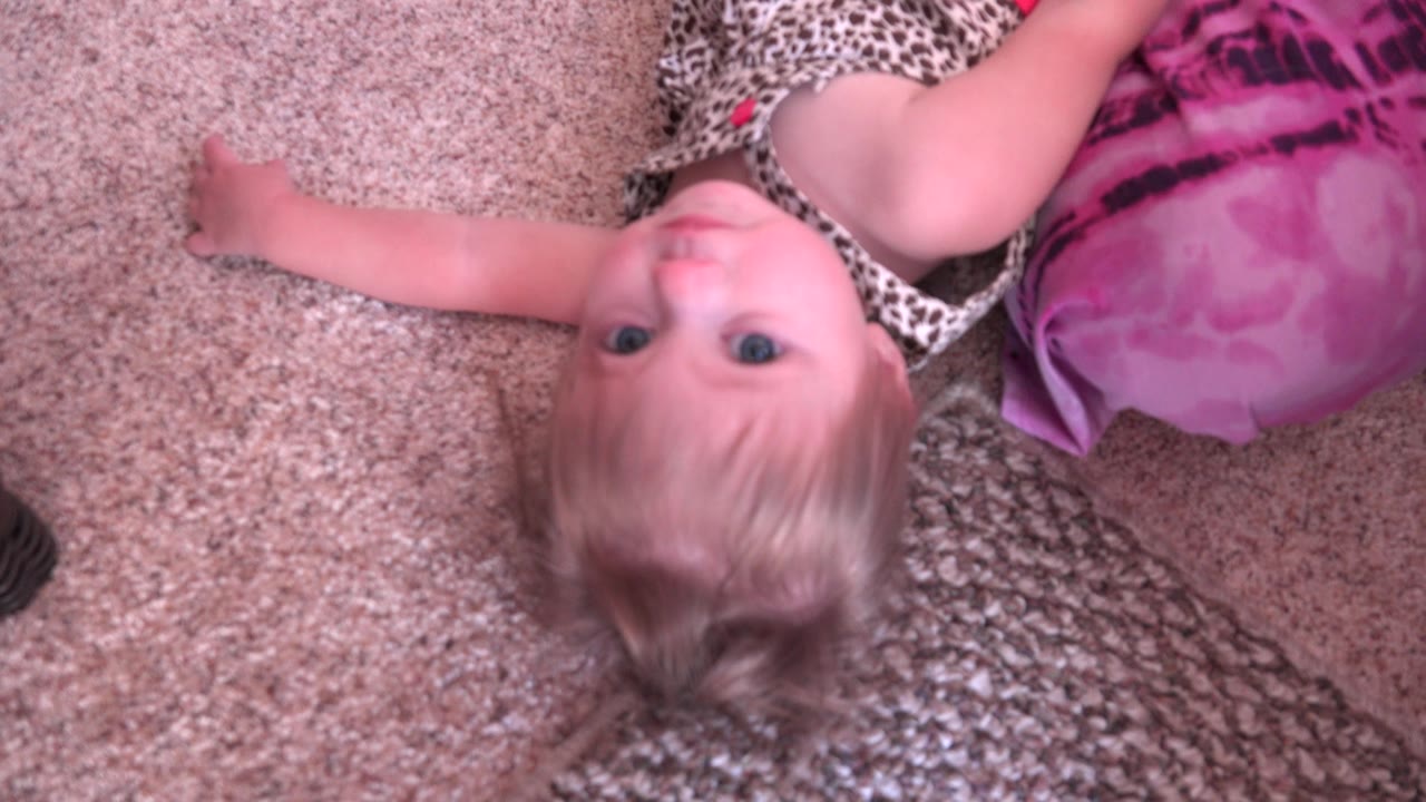 Young girl lying near a pink cushion with her face turned upward.