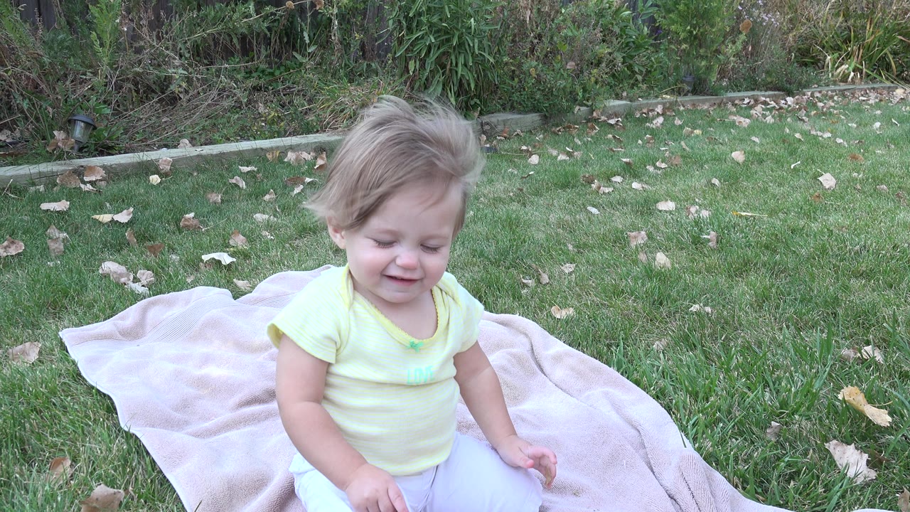 Toddler smiling while seated on a backyard blanket.