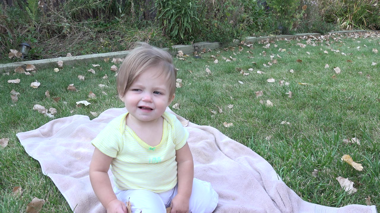 Young girl sitting on a pale blanket in grass.