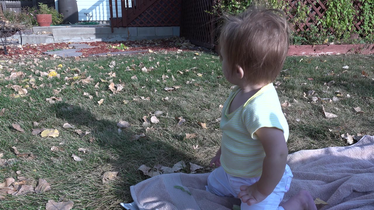 Child turned away while sitting on a towel in the yard.