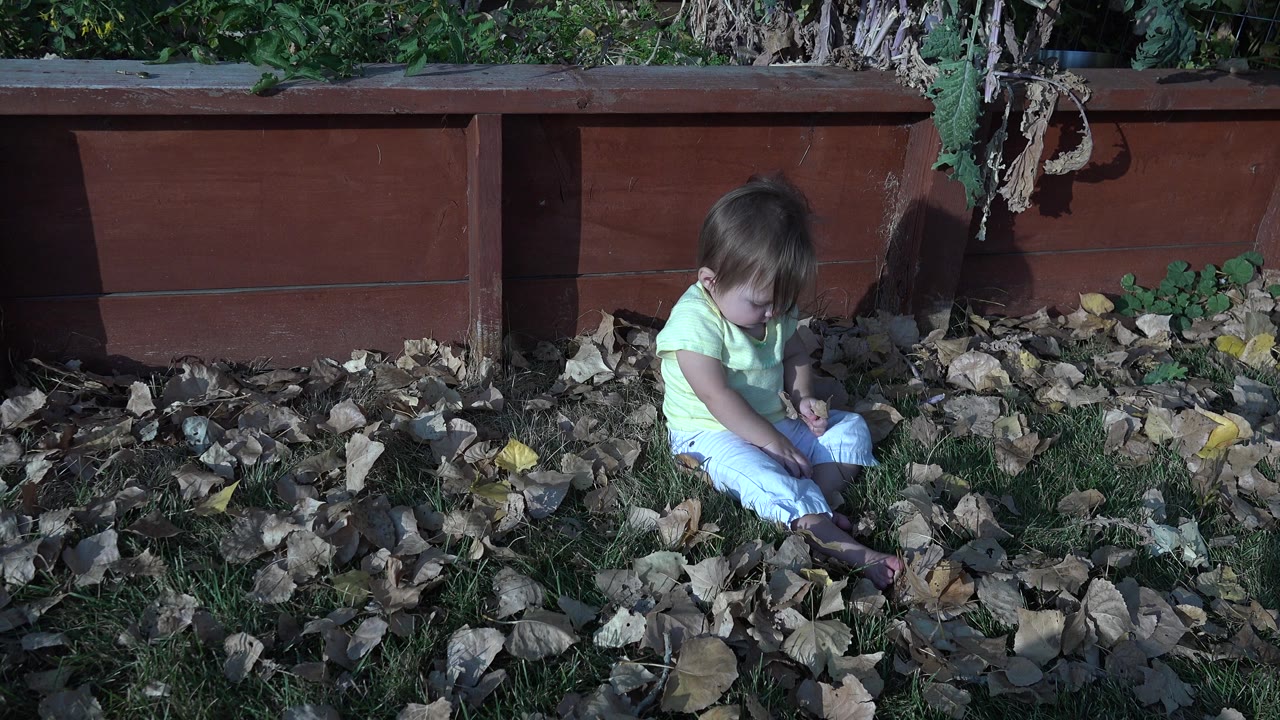 Baby seated near dry leaves with head tilted downward.