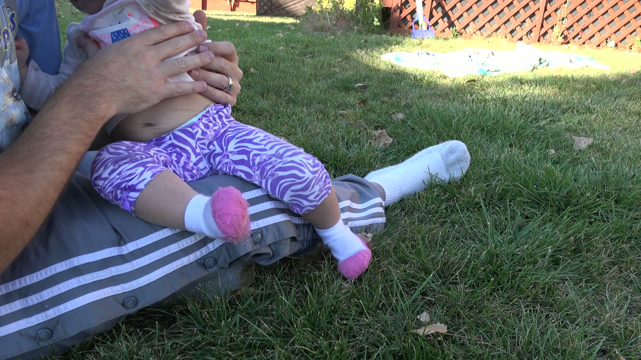 In Westminster, Colorado, the toddler remains on the adult's lap with the adult's hands around the child's torso and legs centered over gray striped pants.