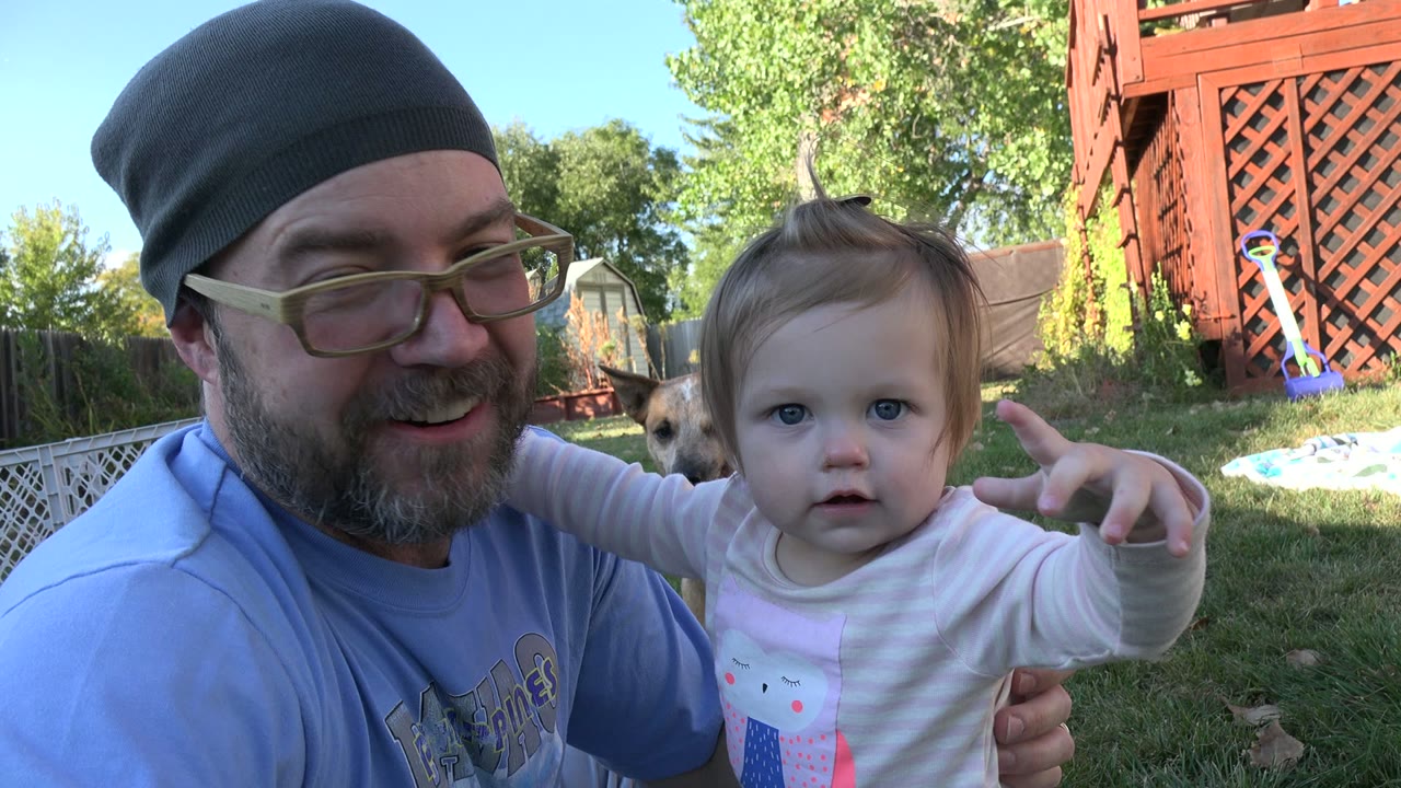 Man and small child face the camera as a dog appears behind them.