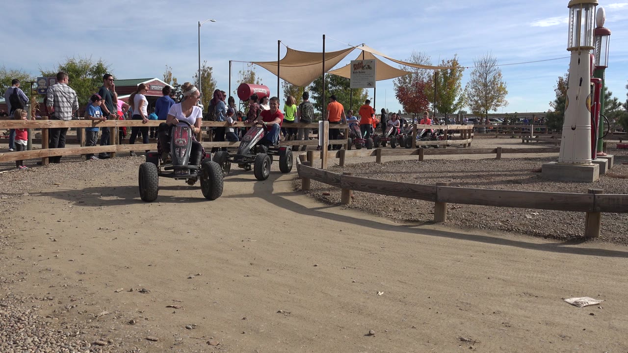 Pedal go-kart on a dirt track near spectators and wooden fencing.
