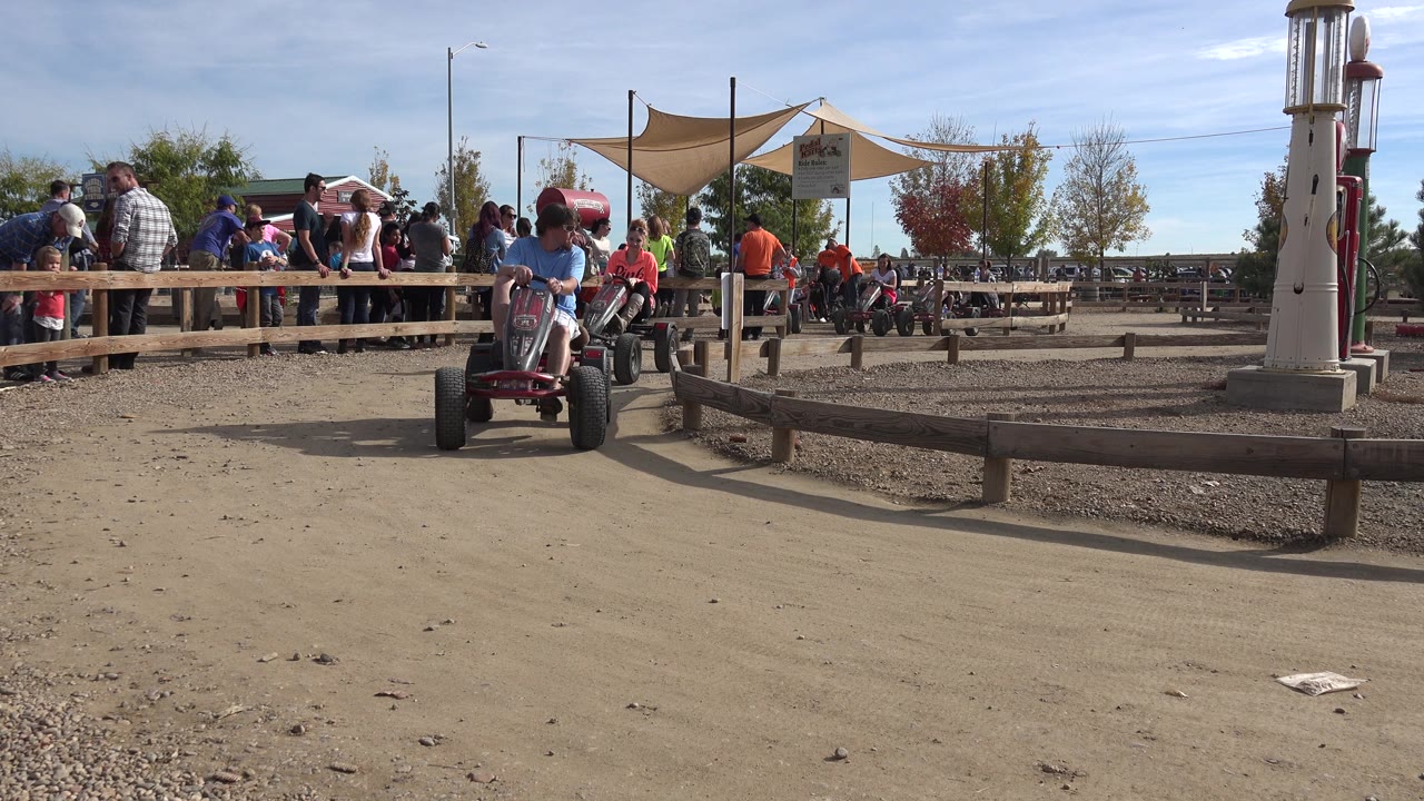 Adult rider turns a red pedal cart toward the camera near a wooden border.