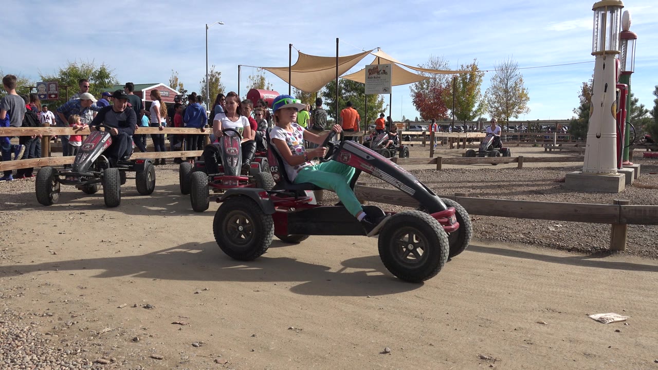 Multiple riders on pedal go-karts moving across a dirt track.