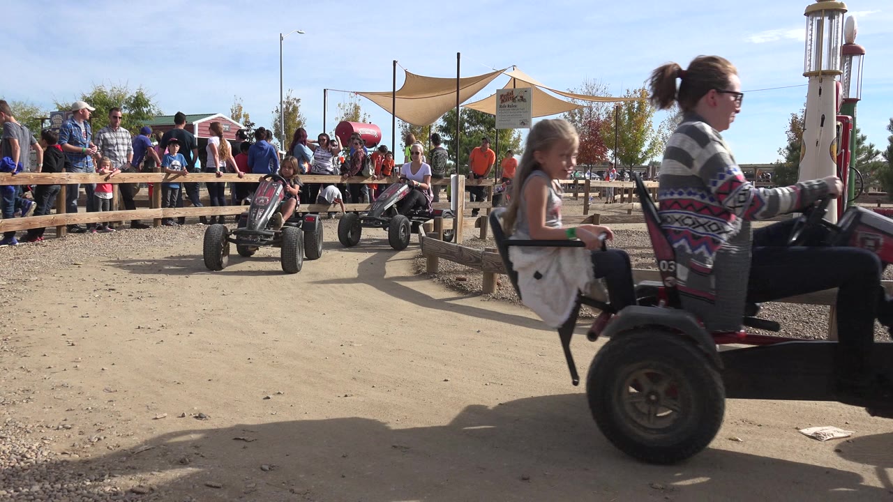 Adult and child pass the camera on a pedal cart beside a fenced track.