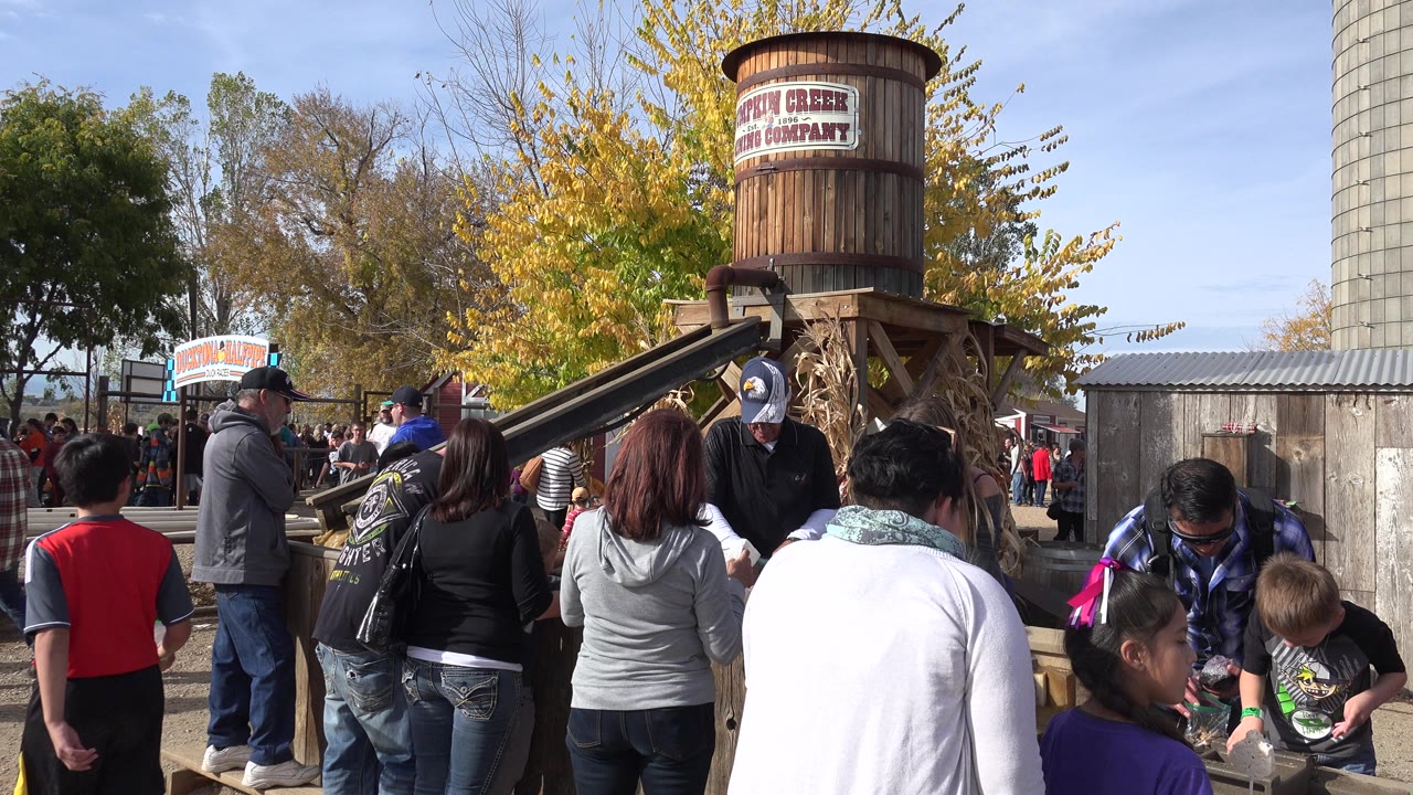 Families gathered around a wooden amusement park attraction with a barrel overhead.