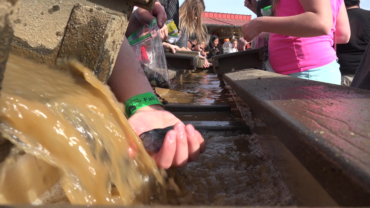 Muddy water pours beside hands and a trough at a crowded outdoor activity.