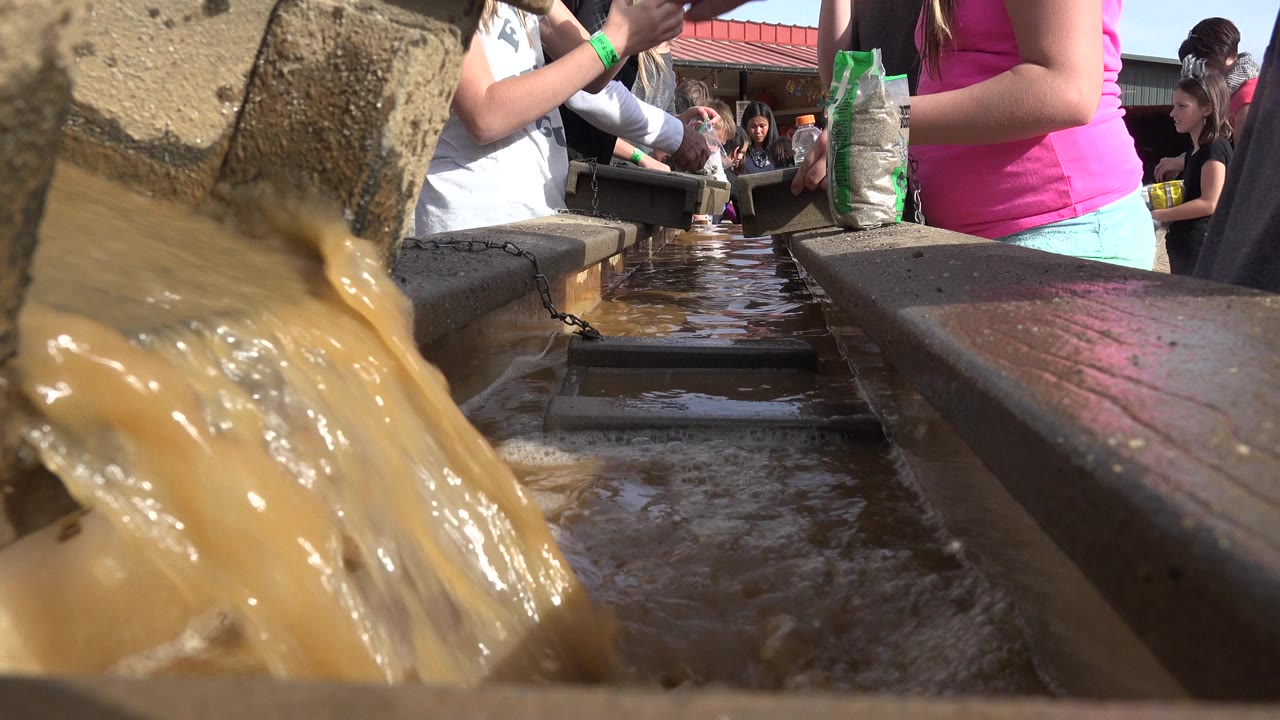 Muddy water flowing through a low trough with people behind it.