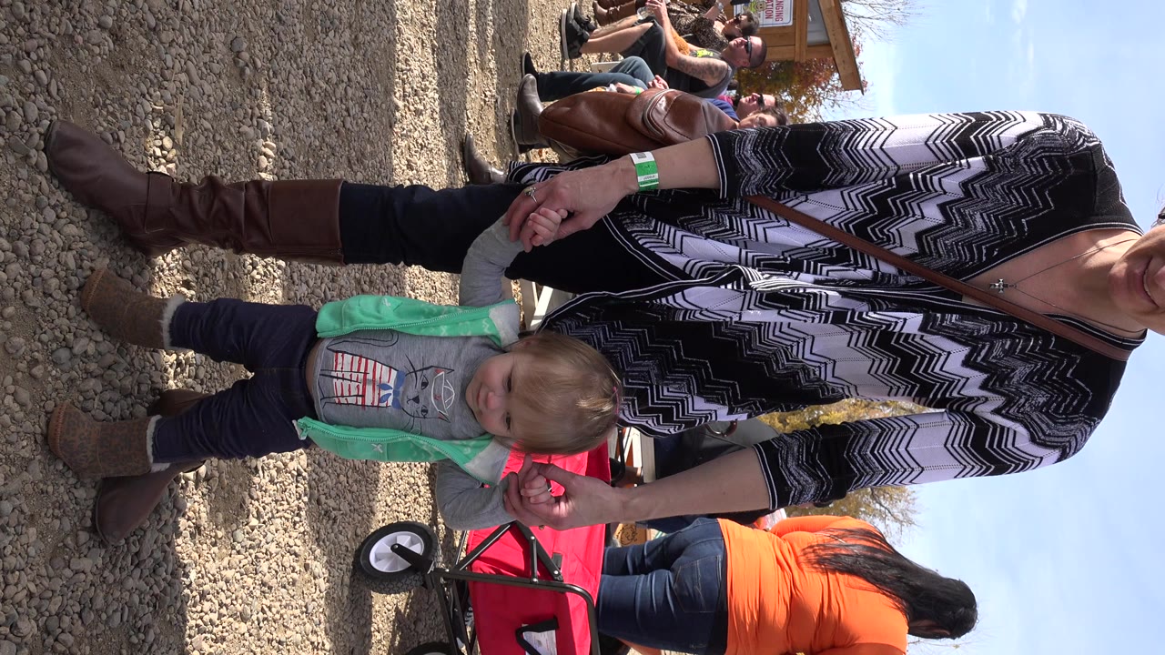 Toddler standing on gravel while an adult holds his hands near a red wagon.