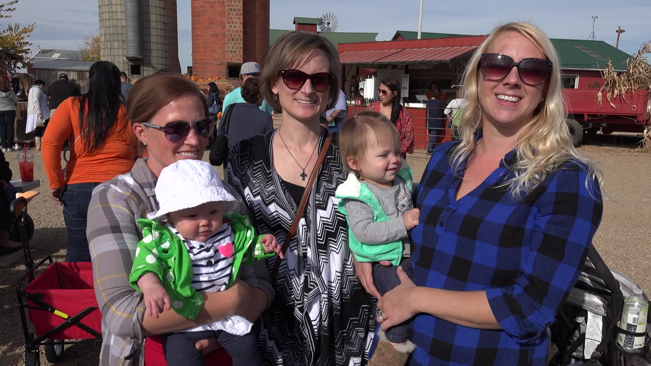 Three women in sunglasses hold two young children outdoors.